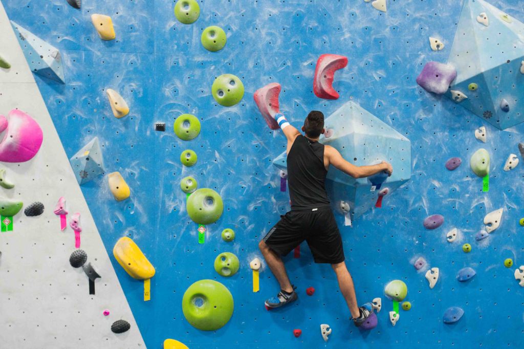 Matthew climbing on a colorful rock climbing wall, where he is reaching for a hold with his residual limb.