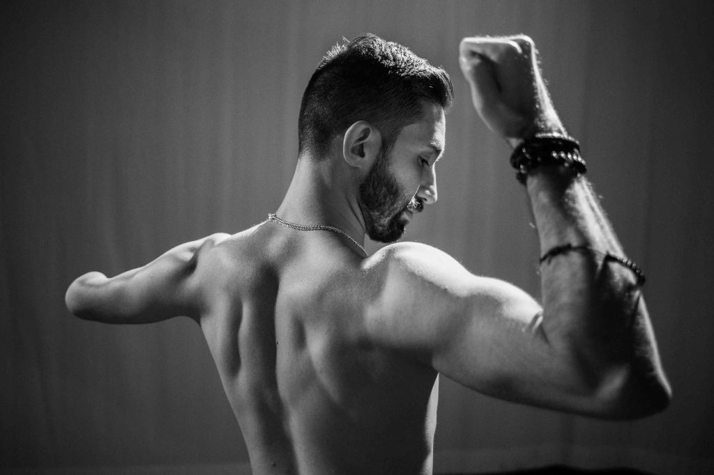 A photo of Matthew from the back, where he is flexing to show well defined back muscles.
