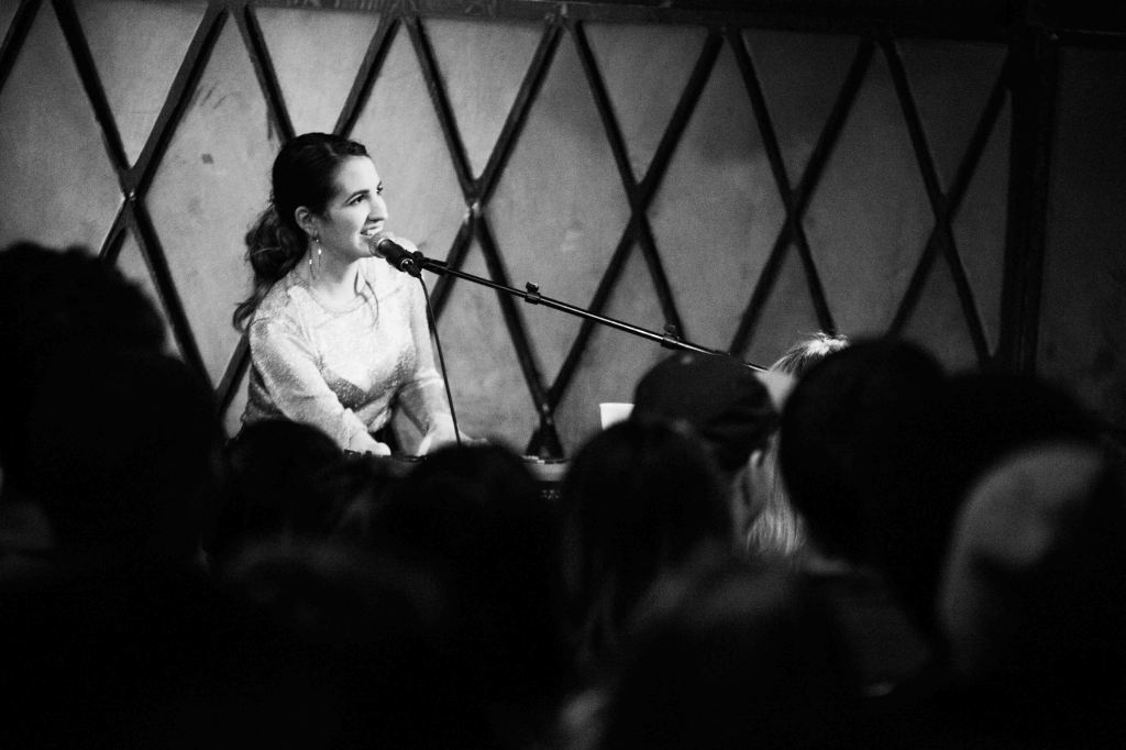Victoria in front of an audience, on the keyboard and smiling while in front of a mic.