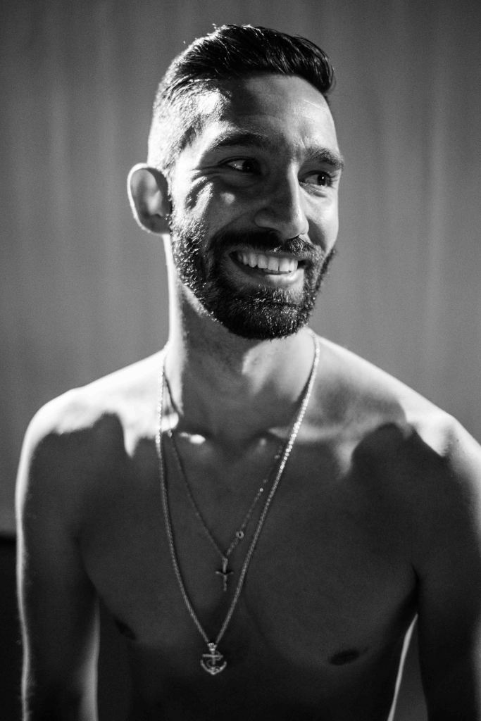 A black and white photo of Matthew smiling, with high contrast due to the lighting in the studio.